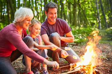 Multi-generation family roasting marshmallows at campfire in forest