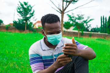 young black man wearing a nose mask, sitting down and using his smartphone