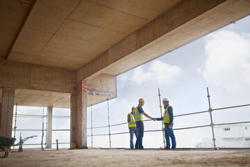 Fototapeta premium Construction workers handshaking at highrise construction site