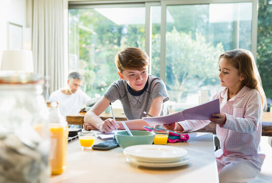 Brother and sister eating breakfast and doing homework
