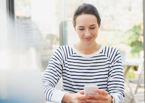 Smiling woman using cell phone at sidewalk cafe