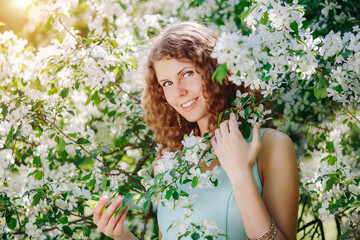 Beauty young happy woman in a flowered garden. Girl among the flowers of apple trees, cherries. Springtime scene. Positive model in a casual style. Lifestyle