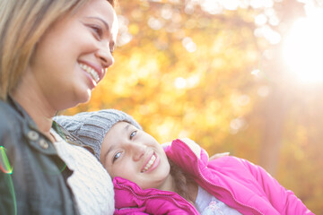 Portrait affectionate mother and daughter below autumn leaves