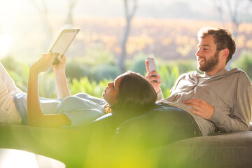 Couple laying and using digital tablet and cell phone on sunny patio