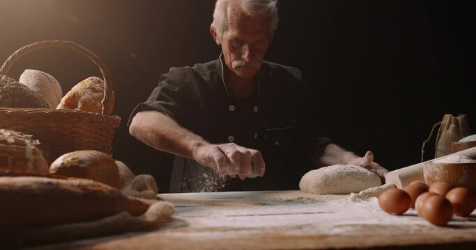 Professional mature caucasian baker putting flour on loaf of bread dough with passion, retired pensioneer enjoying his new hobby, isolated on black background 4k footage