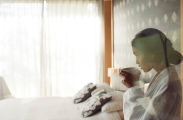Woman in bathrobe sipping coffee in bedroom