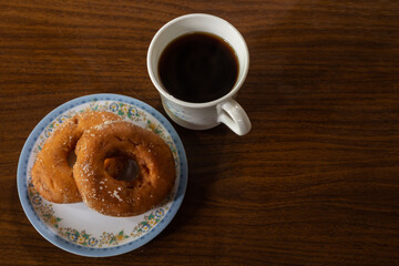 cup of coffee with donuts on saucer on a rustic wooden table