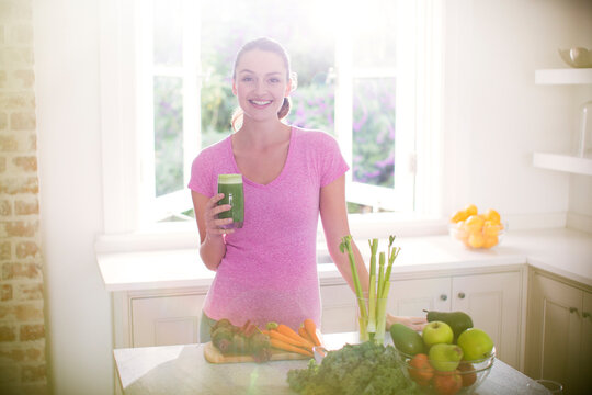 Portrait smiling woman drinking green smoothie in kitchen