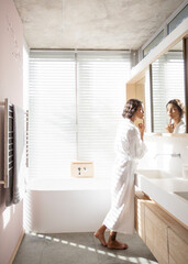 Woman in bathrobe examining face in bathroom mirror