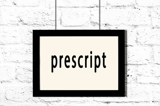 Black frame hanging on white brick wall with inscription prescript