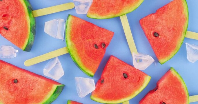 Watermelon slices on sticks with ice cubes. Fresh watermelon popsicles on blue background.