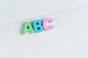 Close up Multicolored wooden letters with ABC on white wooden background. Set of toys for studying alphabet. Education, back to school concept. Top view, copy space