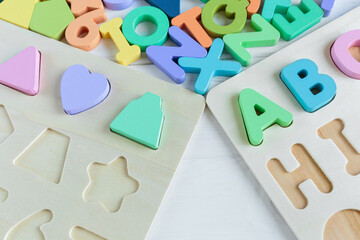 Naklejka premium Close up Multicolored wooden letters with ABC on white wooden background. Set of toys for studying alphabet. Education, back to school concept. Top view, copy space