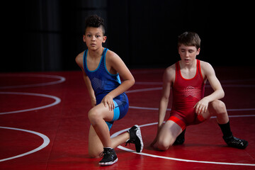 Wrestlers in red and blue singlets practicing on a red mat. 
