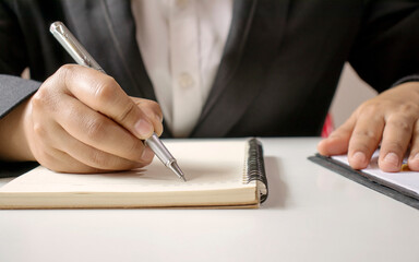 Close-up of a businesswoman using a pen to write a wooden desktop notebook and a memo list.