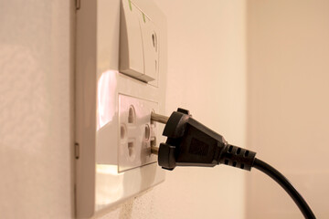 The dangers of using electricity in your home or office, including black hands that are not completely plugged into the white wall.