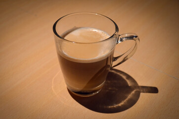 A cup of coffee with milk, over a wooden table. Smooth spot-light pointing to the cup.