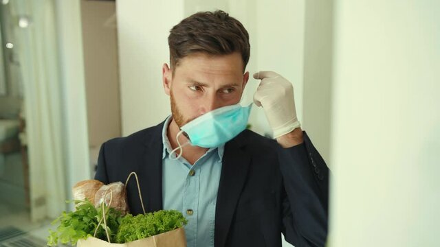 Attractive stylish man coming back home after food shopping entering house taking off mask package pandemic protection quarantine infection social distance returning virus self-care covid-19 slow