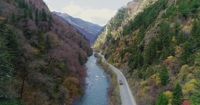 aerial photography and overlook of running car beside flowing river in a beautiful vally in Asia China moving shot of mountain winding highway along with running water with autumn woods