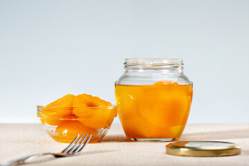 Peach compote in glass bowl with fork. Canned peach halves in jar.