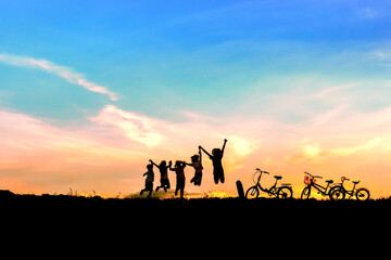 Silhouette of children friends jumping in sunset sky background