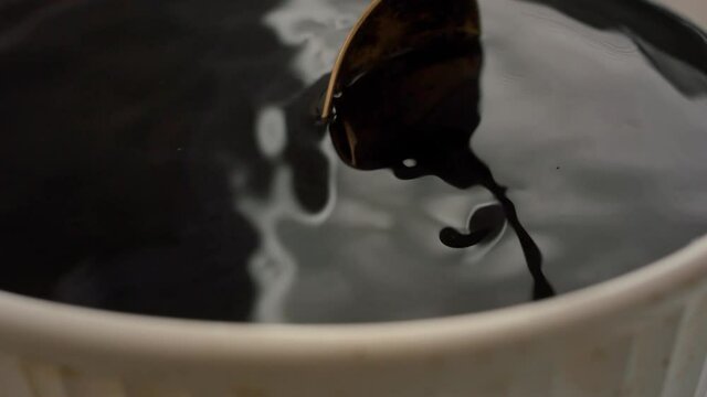 A gold antique spoon stirs a mysterious black potion in a white bowl
