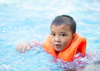 Asian boy in swimming suit and life jacket swimming in the pool