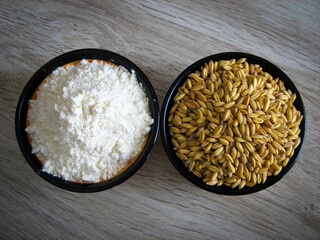 Whole wheat and flour wheat in bowl on wooden table. Close up of wheat grains and wheat flour. Background.