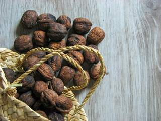 Walnuts scattered from the small wicker basket on  wooden table. Close-up. Walnuts are 4 water, 15 protein, 65 fat and 14 carbohydrates, including 7 dietary fiber.