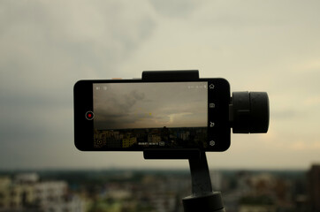 Savar, Dhaka, Bangladesh-June 5, 2020:  Mobile phone Google pixel 3A is shooting a video using gimbal dramatic sky with clouds background is bokeh in the afternoon after raining Video filming concept.