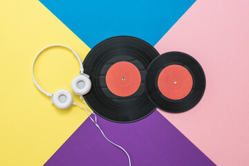 Two vinyl discs and white headphones on a multicolored background.