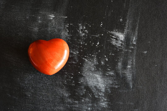 A close up image of red jasper heart shaped crystal on a black and white background. 