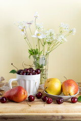 Still life with ripe pears, cherry and wild flowers on wooden table. Cozy background with morning soft lighting