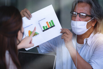 Close up, Asian men and women with protective masks consult the job in a coffee shop, with table shield partition to protect infection from coronavirus covid-19 on table, social distancing concept