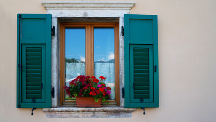 Fototapeta na wymiar A blank pastel wall of a residential building window with shutters and flower pot in Italy with copy space.