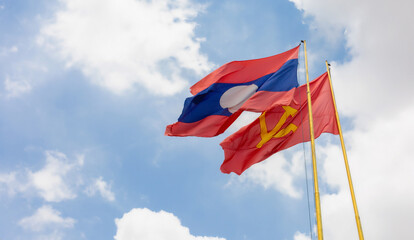 The Lao National Flag with the red flag with communist symbols of a sickle with a hammer flying in a blue sky