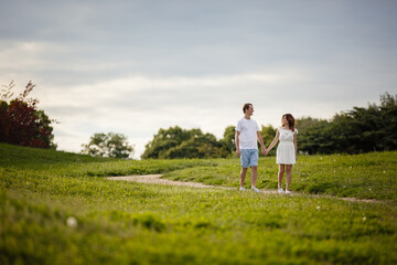 Young man and woman couple walk in the meadow. Tender holding each other. Spring lovestory. Brown-haired girl with curled hairs and man weared in casual and denim. Young family