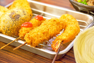 居酒屋のテーブルに並ぶ、大阪名物串カツと鮮やかな緑色のネギの小口切りをたっぷり天盛りにした牛すじとこんにゃくの味噌煮込み、どて煮。Osaka specialty deep-fried skewered meat and vegetables & Doteni (Beef Tendons Simmered in miso)  ,Stewed Beef Tendon.