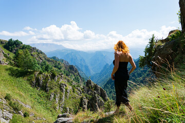 Fototapeta na wymiar A beautiful girl in a black dress with a cleavage, a European woman with red hair, walking barefoot along a mountain range.