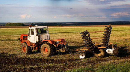  tractor plows and harrows  land in  large field on  sunny spring day. preparing  soil for planting...