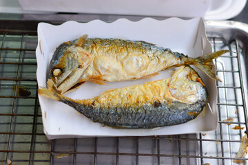 mackerel fish were cooked by frying, Two fried mackerel fish for sale in the market, Popular fish menu in Thailand, (close-up, top view), Crispy fried mackerel placed on white paper plate