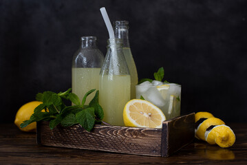 bottles of cold lemonade, fresh lemons and mint in wooden box