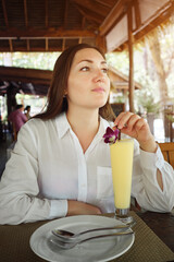 Young brunette woman drinks a fruit cocktail in outdoor cafe.