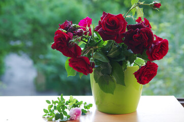 A bouquet of red roses in a green vase standing on a windowsill.