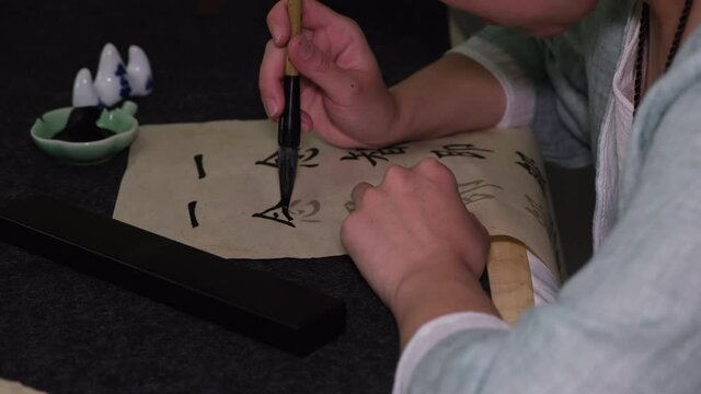 Young woman practicing Chinese traditional calligraphy at home. The Chinese characters mean mind or thinking. 