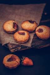 Cupcakes with white cream and strawberry on vintage blanket over black wooden background with fresh strawberries.