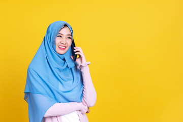 Smiling Asian muslim woman with using mobile or smartphone over isolated color background.