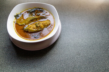 Angle shot of Thai authentic catfish red curry is a popular spicy dish for Thai cuisine. Indian looked curry with catfish, basil leaves, and red pepper  served in white bowl on dining table