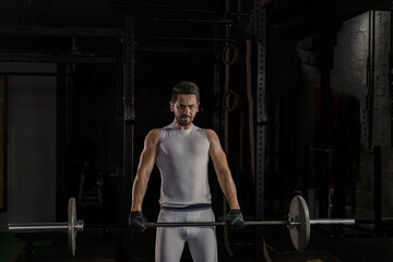 Fototapeta na wymiar Selective focus of good looking young Caucasian sport man doing exercise by weight lifting in a dark gym. White strong man got sweat while lifting weight in gym with shadow background. Body building