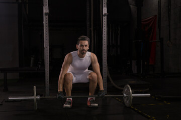 Fototapeta na wymiar Selective focus of good looking young Caucasian sport man doing exercise by weight lifting in a dark gym. White strong man got sweat while lifting weight in gym with shadow background. Body building
